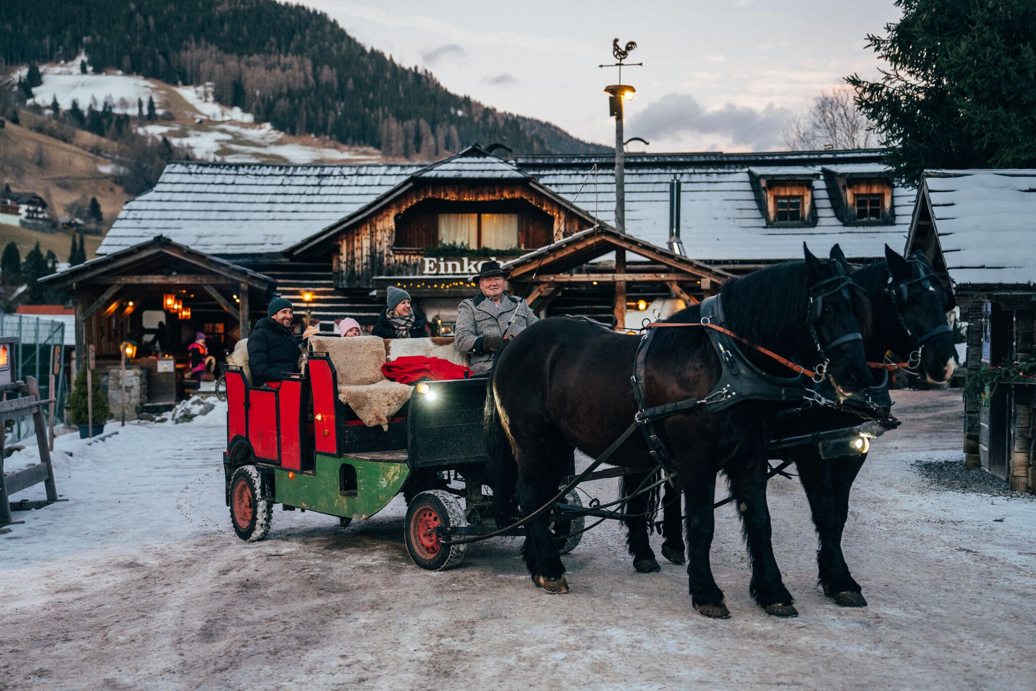 Horse-drawn sleigh with smiling guests in front of a rustic mountain hut in a wintry landscape