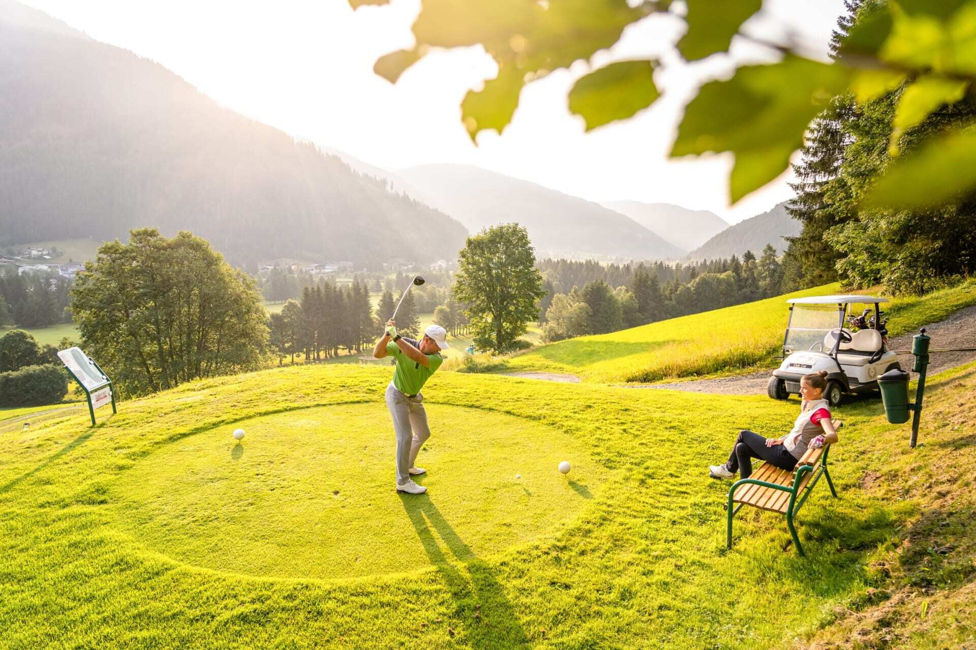 Golfer hits ball on a well-tended green, surrounded by picturesque mountains and trees.