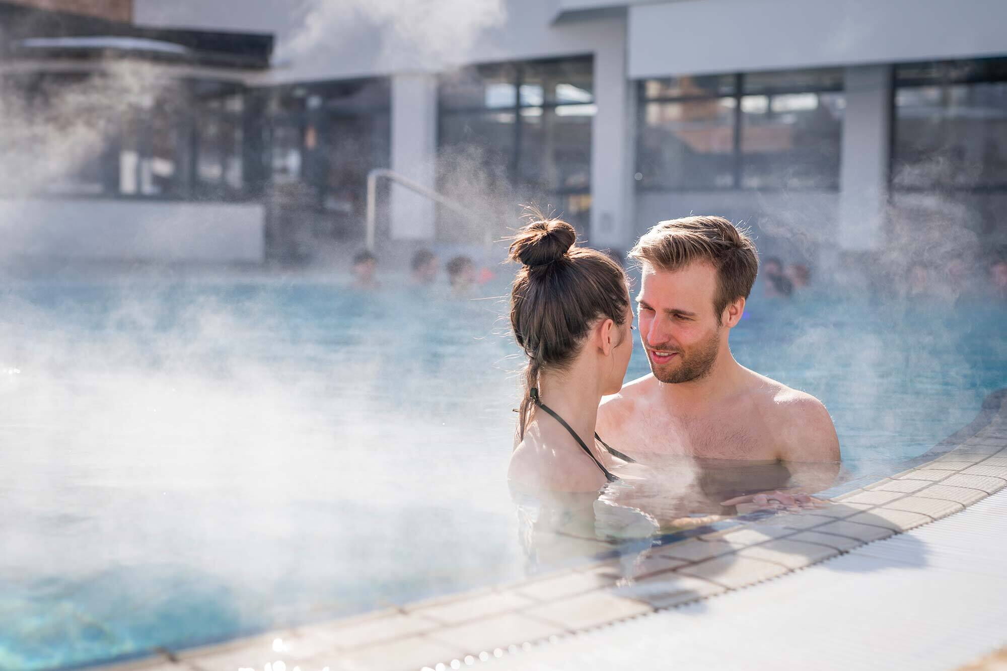 Paar genießt entspannendes Bad im dampfenden Pool an einem sonnigen Tag.