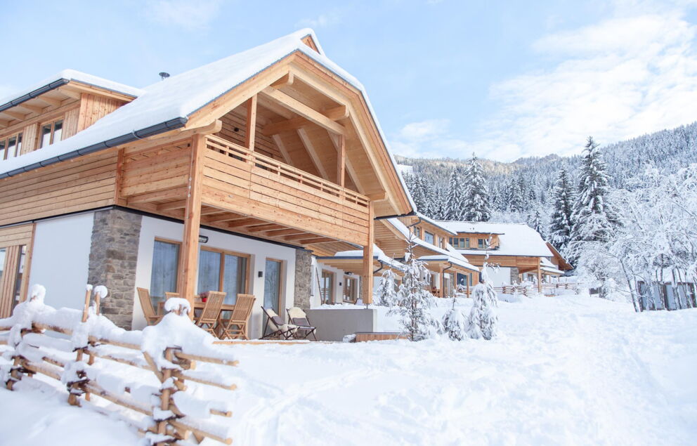 Holzchalets im Schnee, umgeben von verschneiten Wäldern und klarer Winterluft.