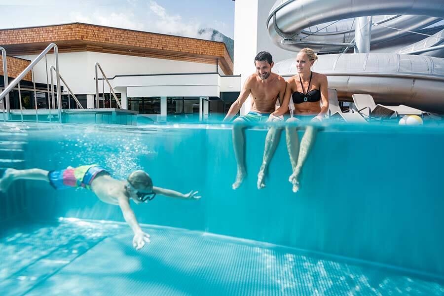 Famiglia che si gode la piscina mentre un bambino nuota nell'acqua con il sole.