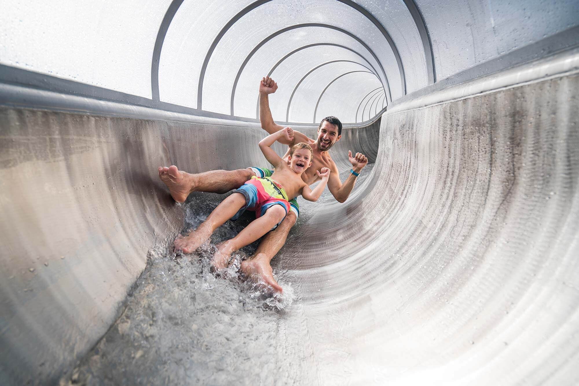 Vater und Sohn rutschen lachend eine Wasserrutsche hinunter