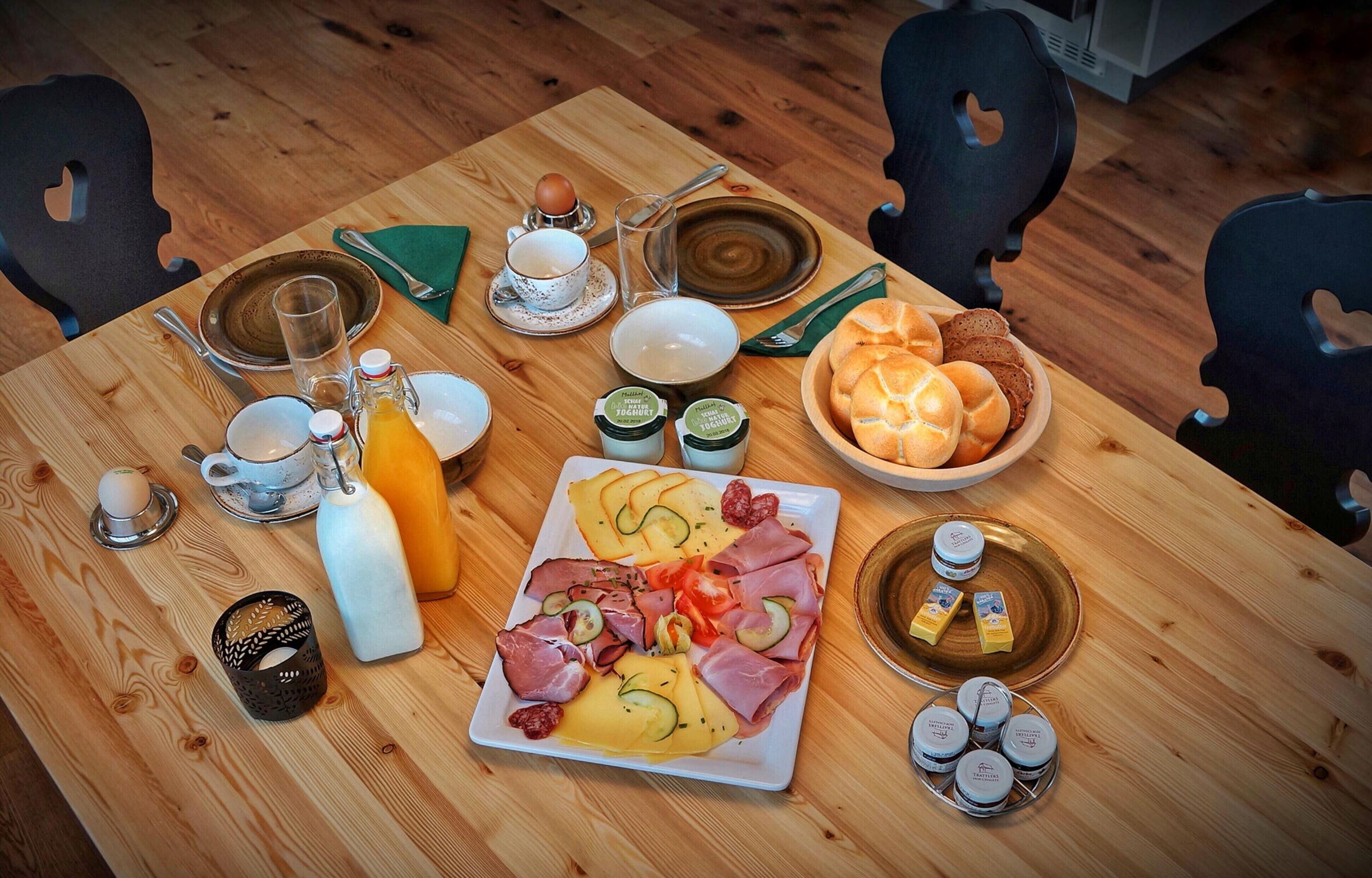 Breakfast table with fresh bread, cold cuts, juices and candlelight on a wooden table