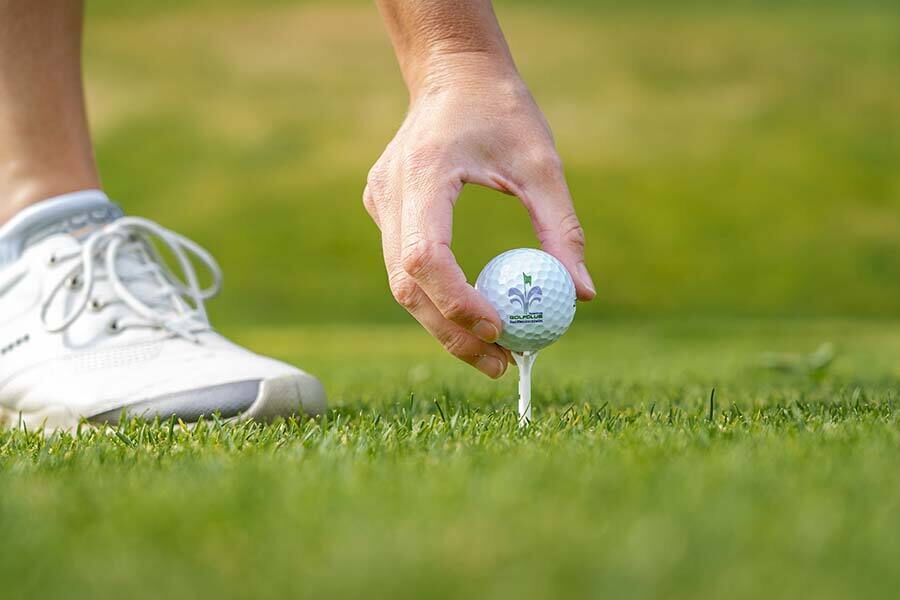 Hand platziert Golfball auf Tee auf grünem Rasen im Sonnenschein.
