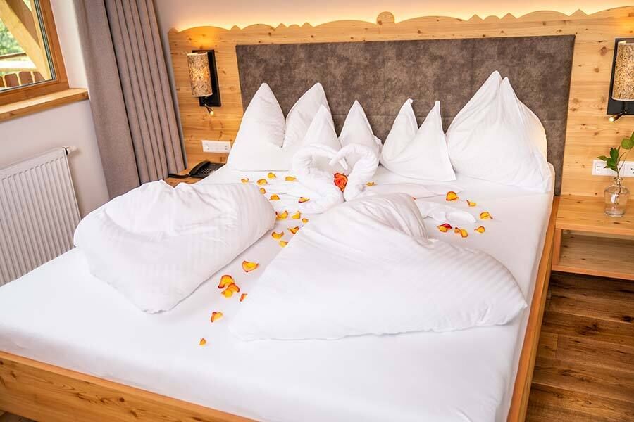 Cozy bed with decorative pillows and rose petals on white bed linen.