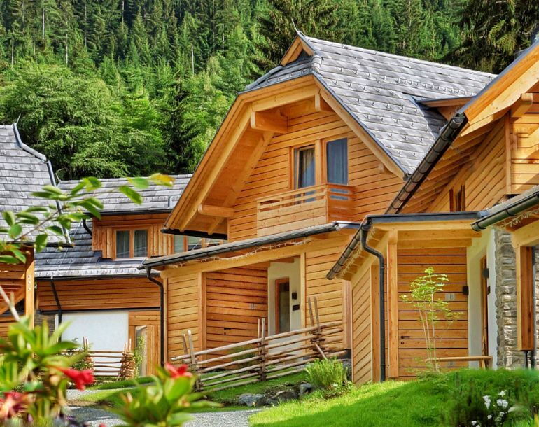 Wooden chalets against a green forest backdrop, surrounded by flowering shrubs and nature.