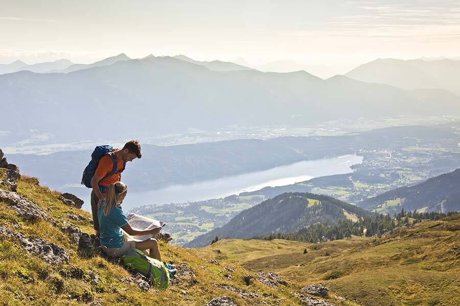 Zwei Wanderer genießen atemberaubende Aussicht über Kärntner Täler und glitzernden See.