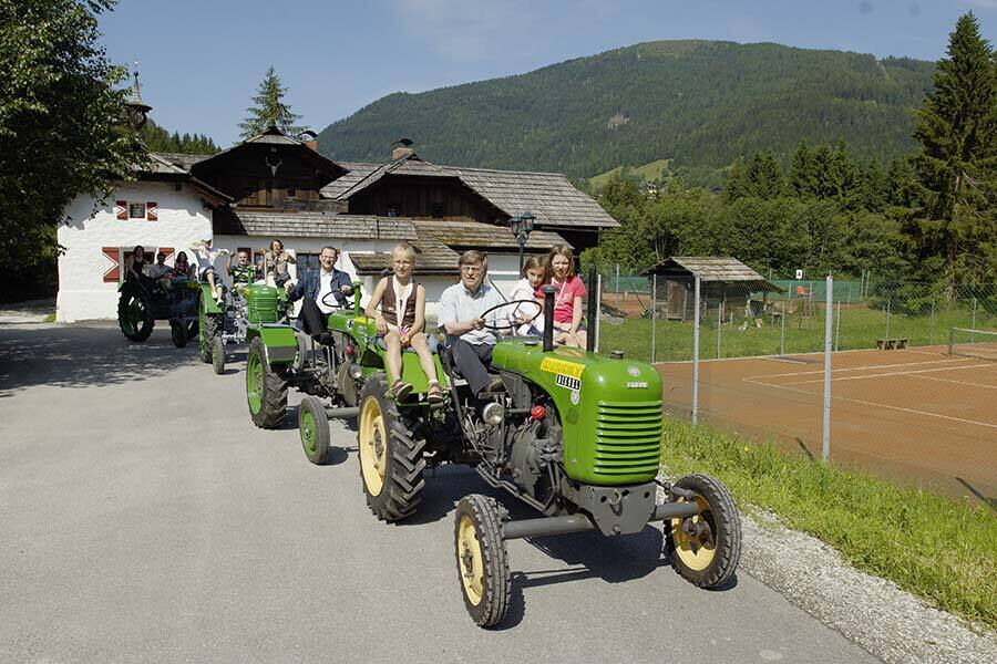 Group rides on classic tractors in front of a rustic chalet through the idyllic Carinthian countryside.