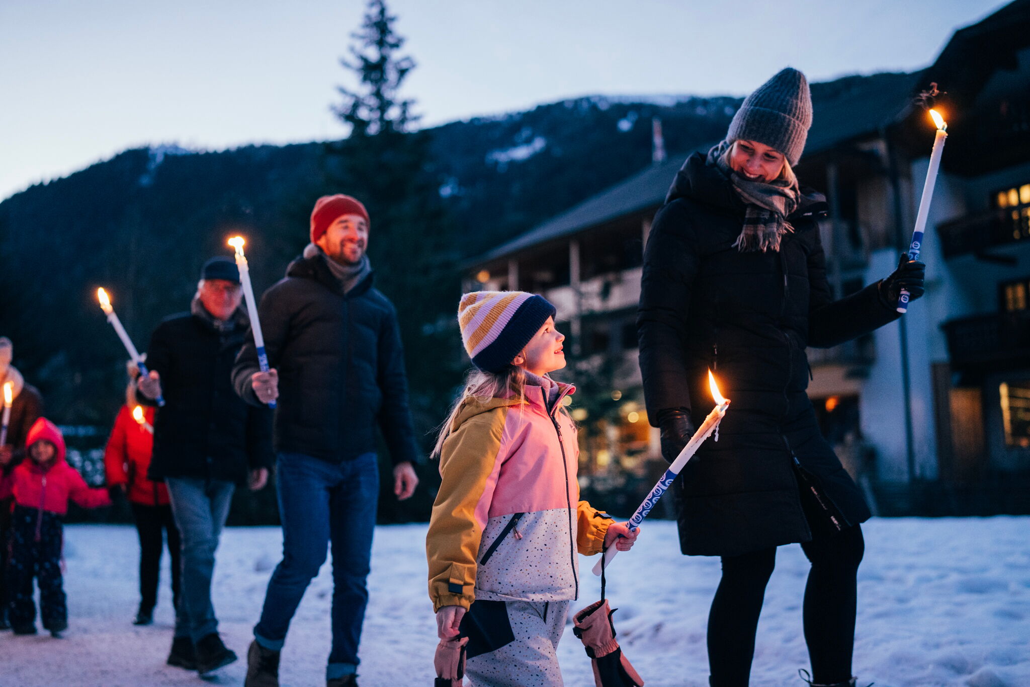 People walking with torches in the snow, smiling and in winter clothing.