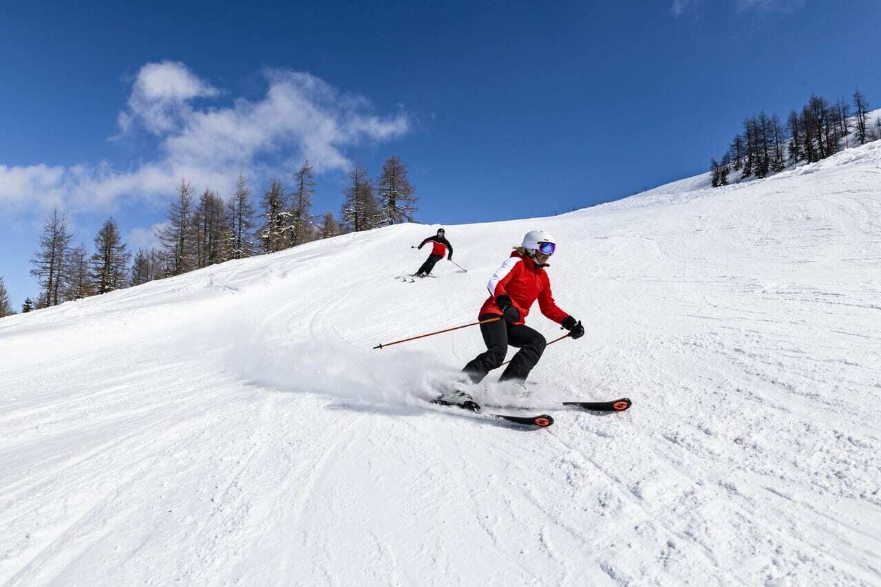 Due sciatori si godono le piste innevate sotto un cielo azzurro.