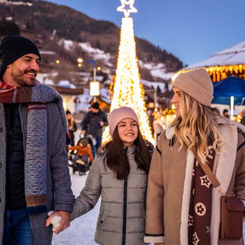 Famiglia sorridente che passeggia in un mercato invernale illuminato a festa.