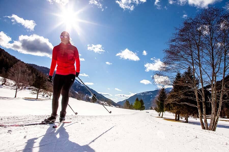 Cross-country skiers in bright sunshine, surrounded by snow-covered Nockberge mountains and blue skies.
