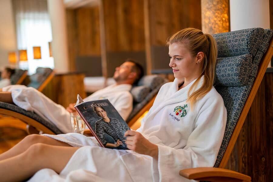 Two people relax in comfortable loungers with magazines in the wellness area.