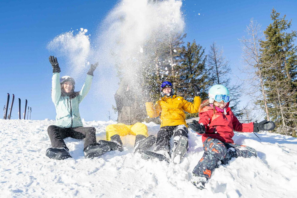 Le persone che ridono gettano la neve in aria in una soleggiata giornata invernale.