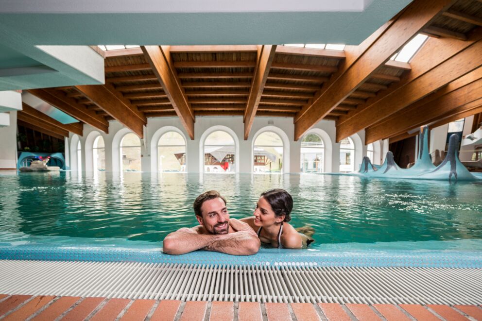 Paar genießt entspannendes Schwimmen in einem eleganten Thermalbad mit Holzdecke.