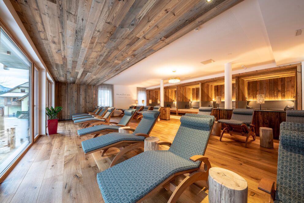Sala relax con comodi lettini, pareti in legno e ampie finestre per la luce naturale.