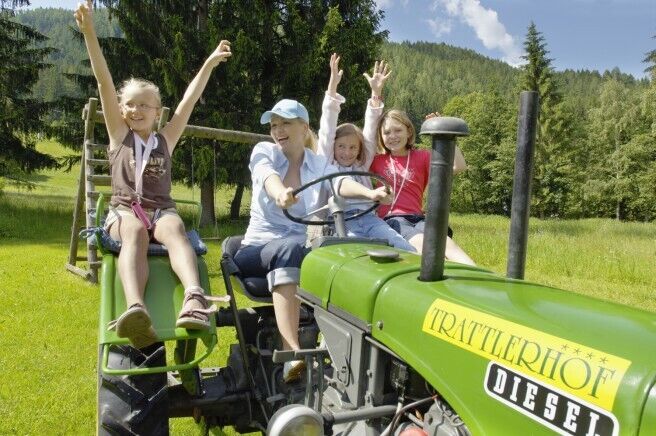 Lachende Kinder auf grünem Traktor im sonnigen Kärntner Bergidyll.