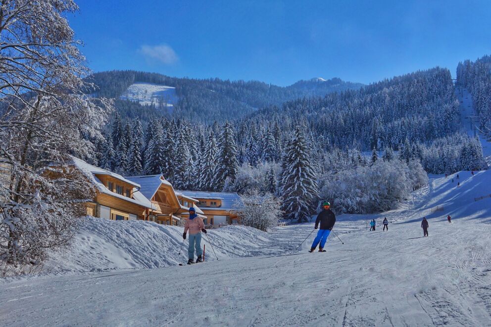 Skiers in front of snow-covered chalets in a picturesque winter landscape with mountains.