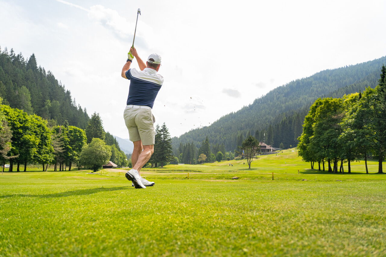 Golfers teeing off on a manicured green against a picturesque mountain backdrop.