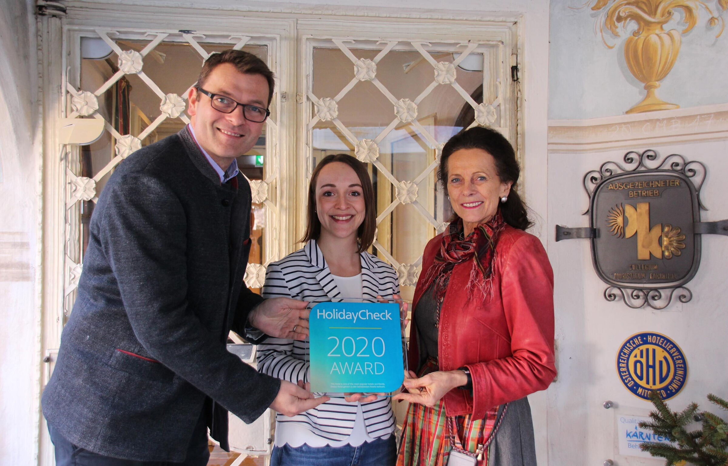 Tre persone con il premio HolidayCheck davanti al premiato hotel carinziano.