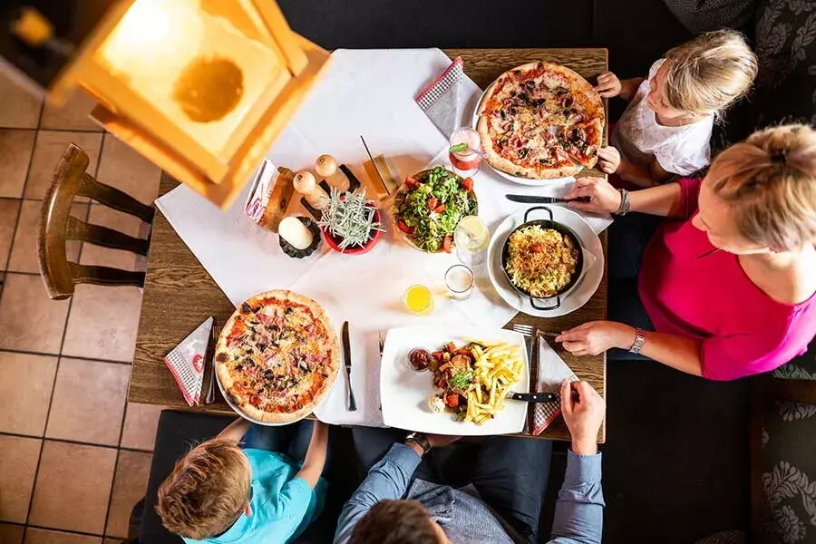 Familie genießt hausgemachte Pizzen und regionale Spezialitäten am gedeckten Tisch.