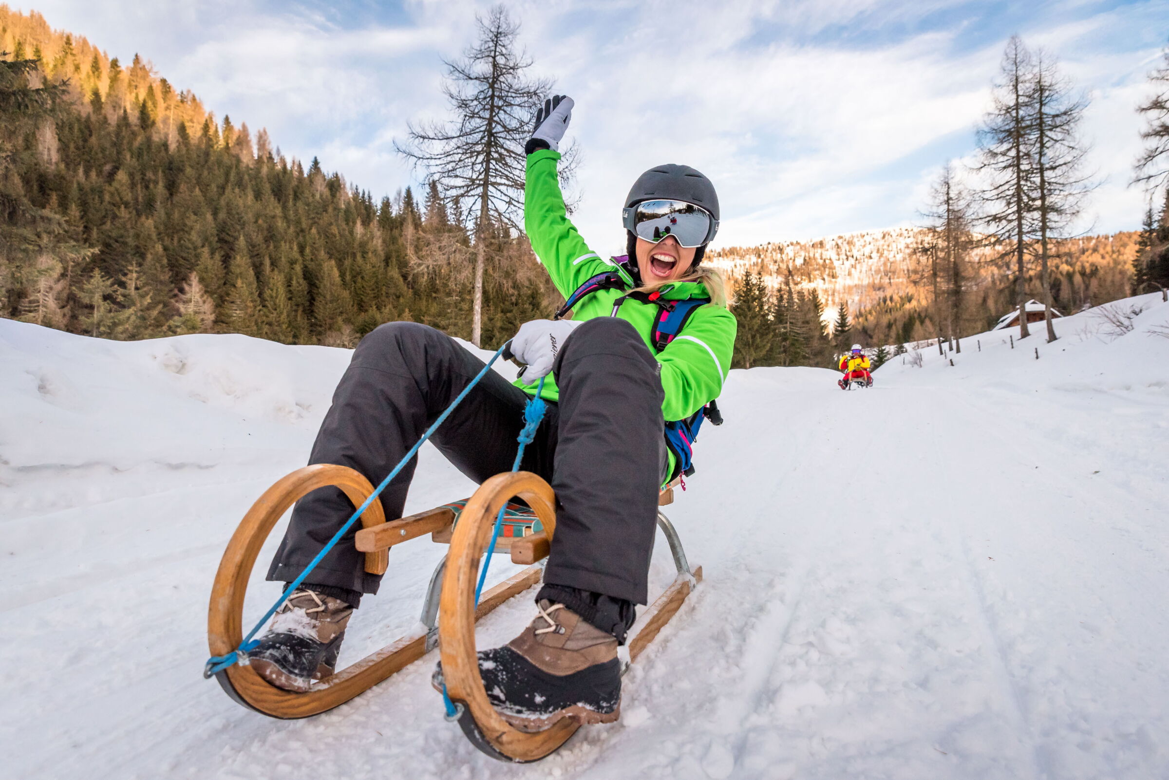 Person joyfully tobogganing on a snow-covered slope in a picturesque mountain landscape.