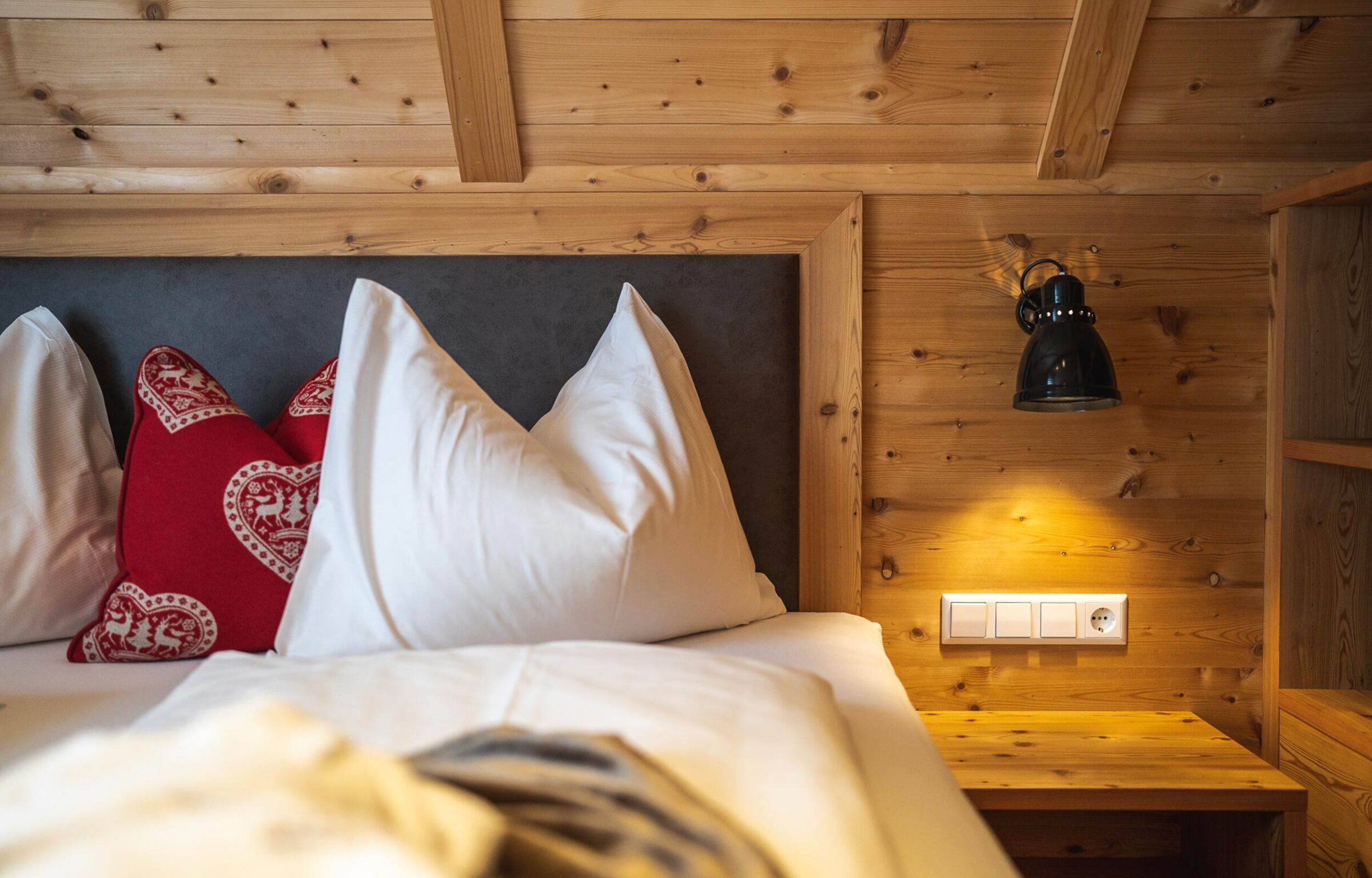 Elegant chalet bedroom with wooden walls, white cushions and red decorative pillows.