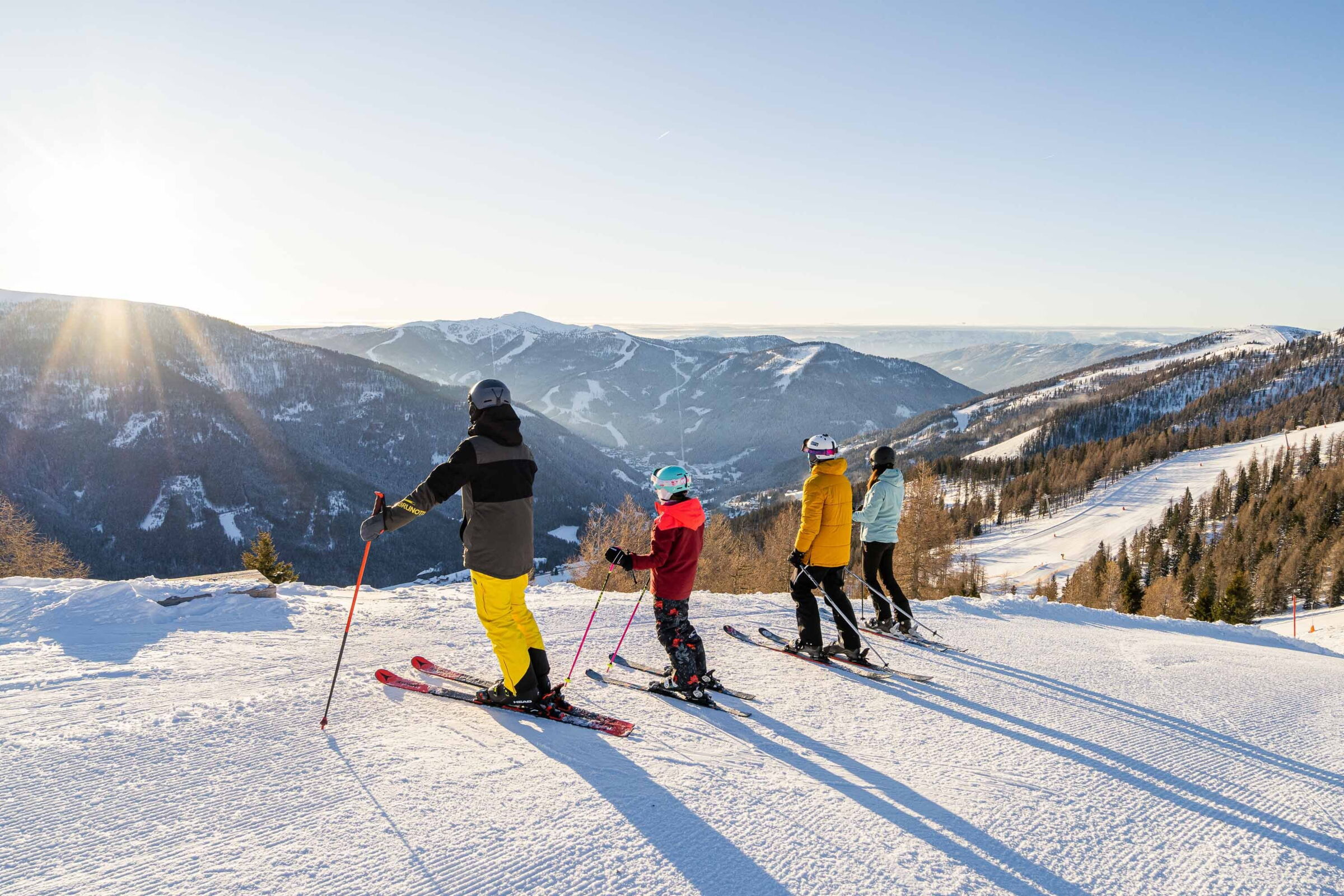 Skiurlauber genießen die Aussicht auf schneebedeckte Berge bei Sonnenaufgang in Kärnten.