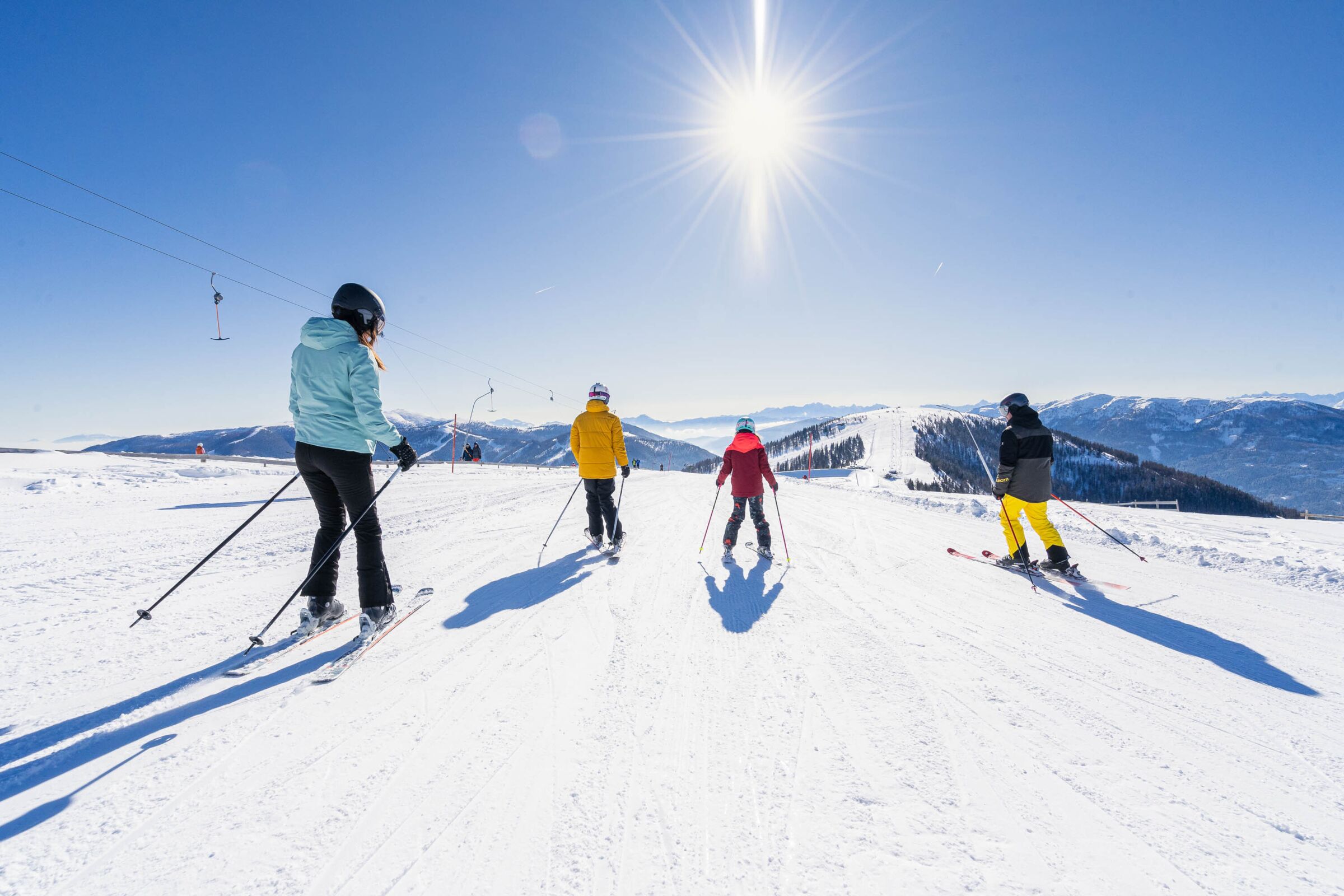 Famiglia che si diverte a sciare sotto il sole splendente nelle montagne innevate dei Nockberge.