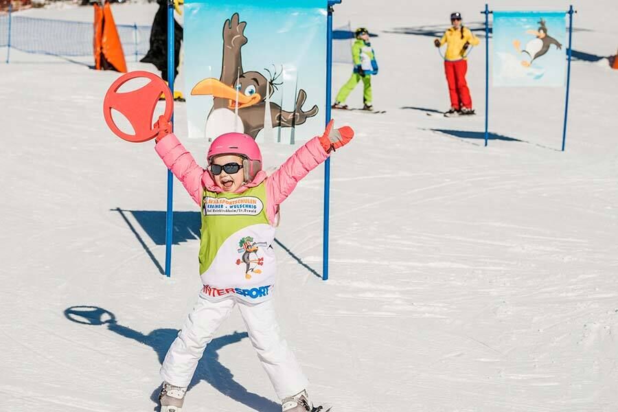 Un bambino raggiante sulla neve, allegro con l'attrezzatura da sci su uno sfondo colorato.