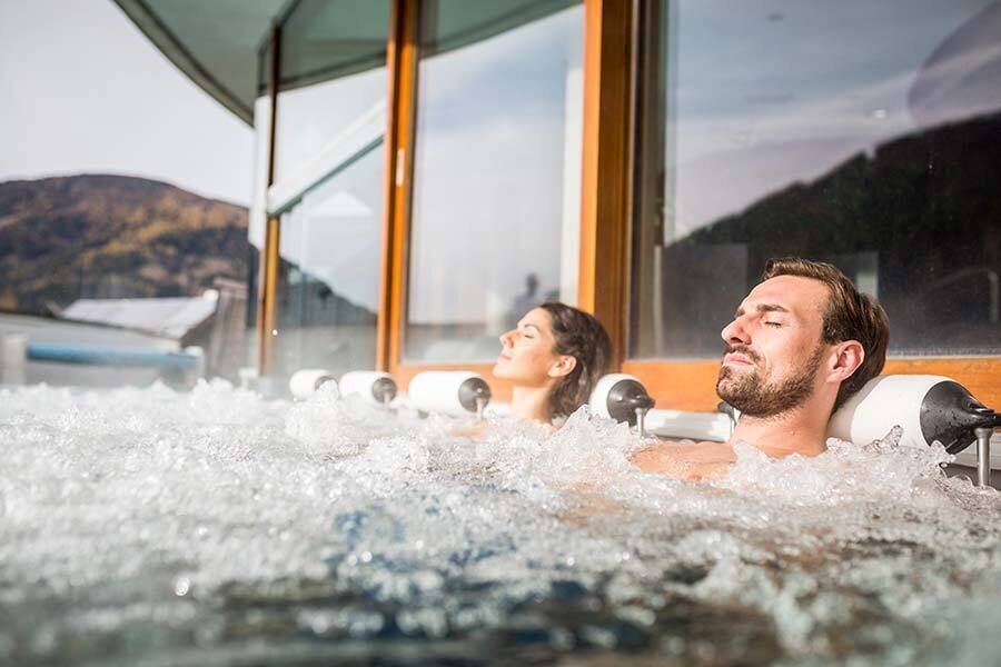 Two people relax in the bubbling water with a mountain view in the background.