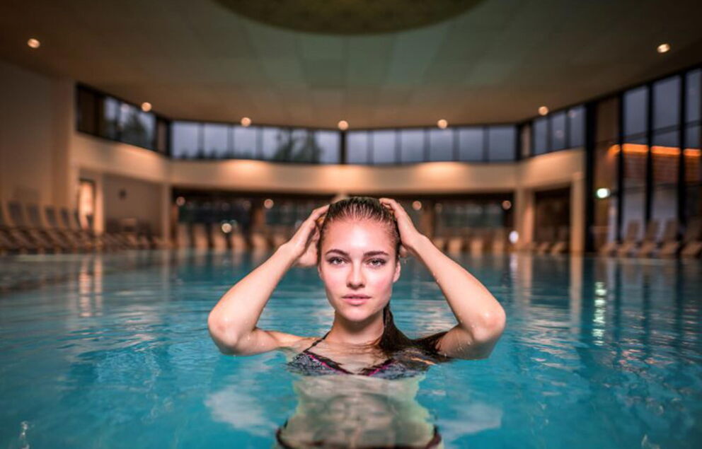 Frau genießt entspanntes Bad im stilvollen, modernen Thermalbad mit großen Fenstern.