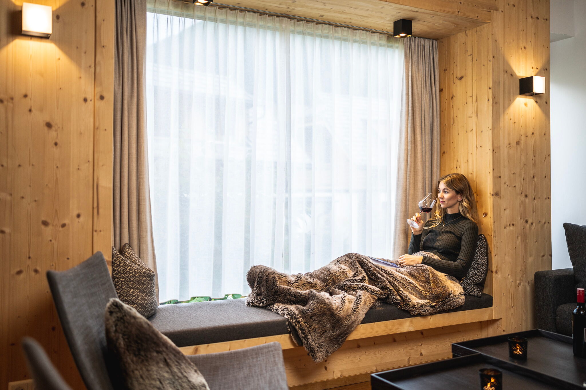 Woman relaxing with wine on a windowsill, wrapped in soft fur in the chalet.