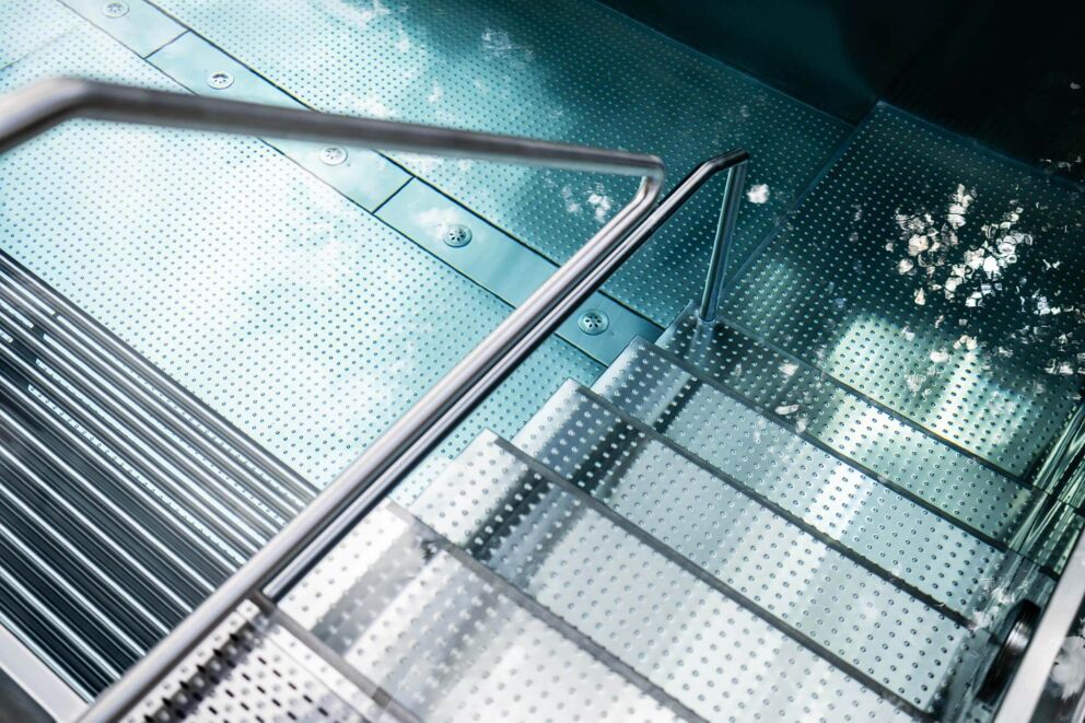 Moderna scala interna in vetro con corrimano in acciaio inox, dal design elegante e chiaro.