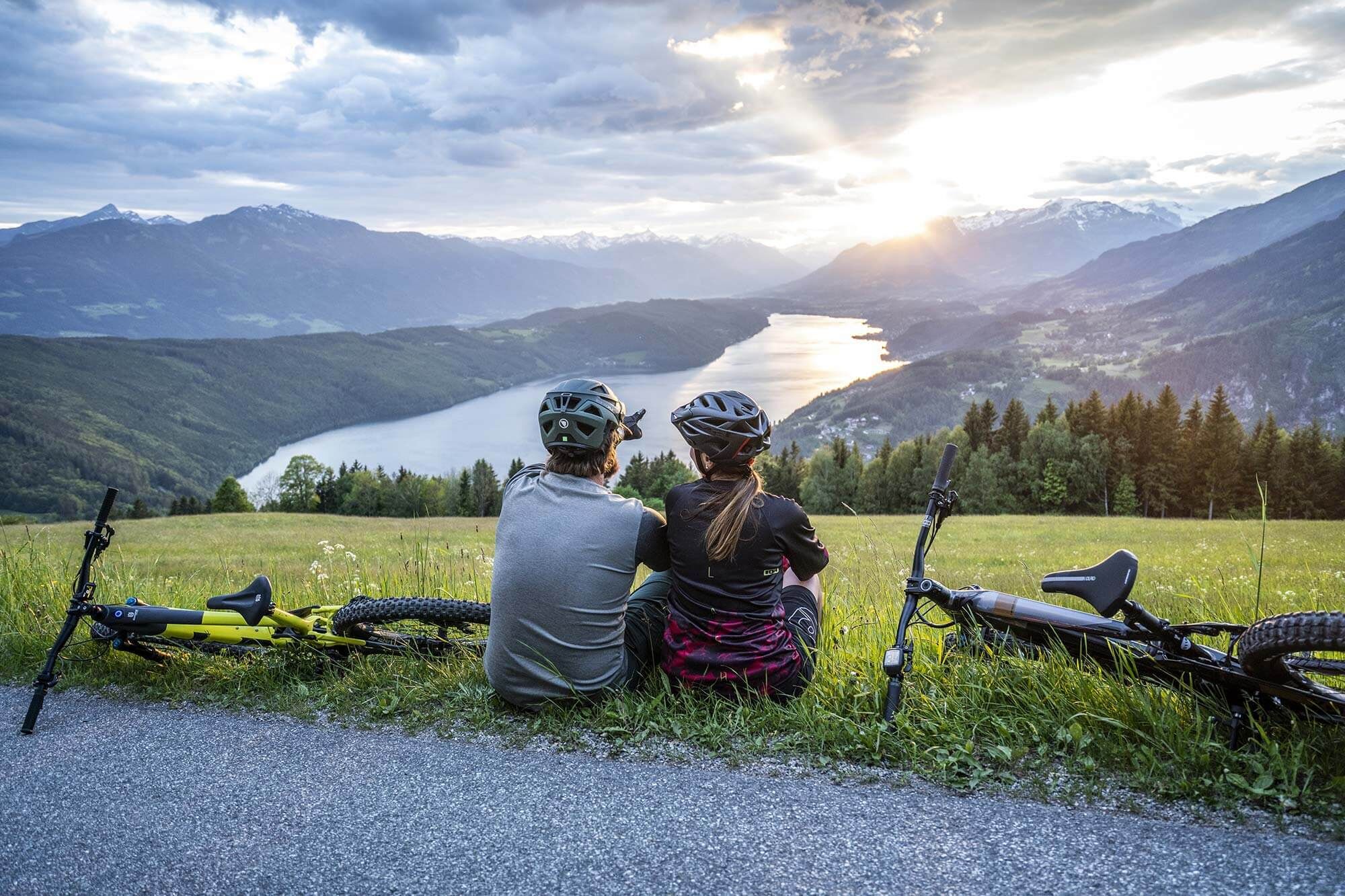 Due ciclisti si godono il tramonto mozzafiato su un lago e sulle montagne.