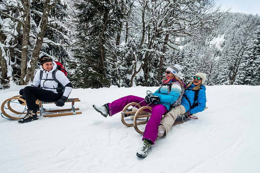 Drei Personen schlittern lachend im verschneiten Wald von Bad Kleinkirchheim.