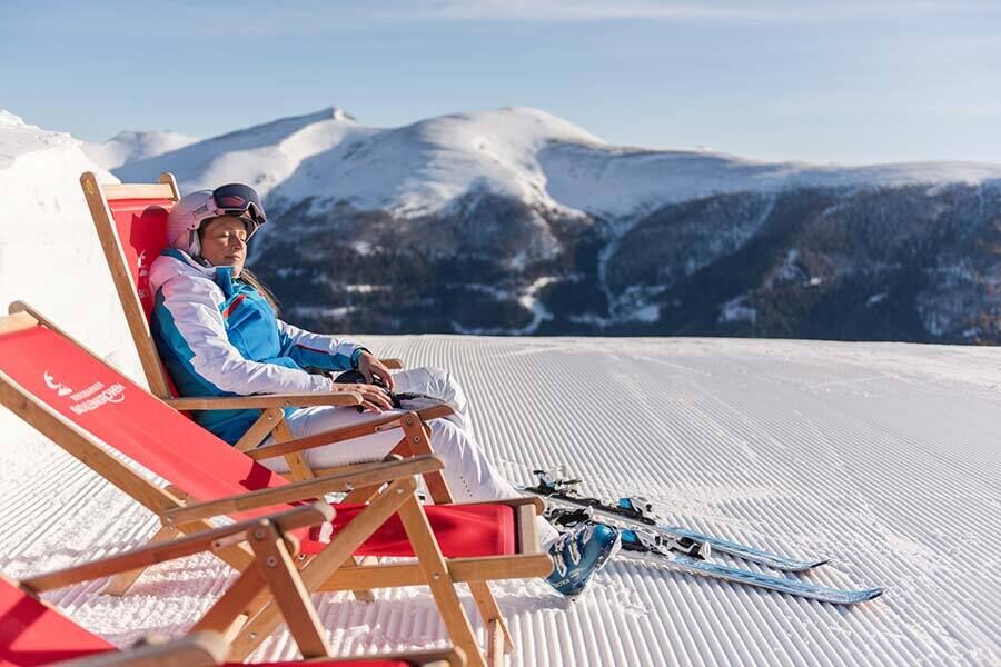 Skier relaxing in a deckchair on a sunny, snow-covered mountain plateau.