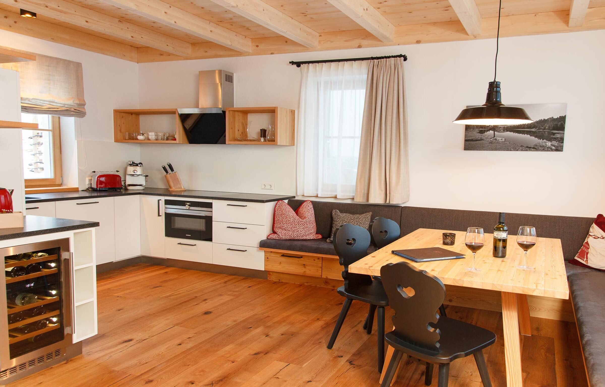 Modern wooden kitchen with sitting area, dining table, chairs and wine glasses in a cozy chalet.