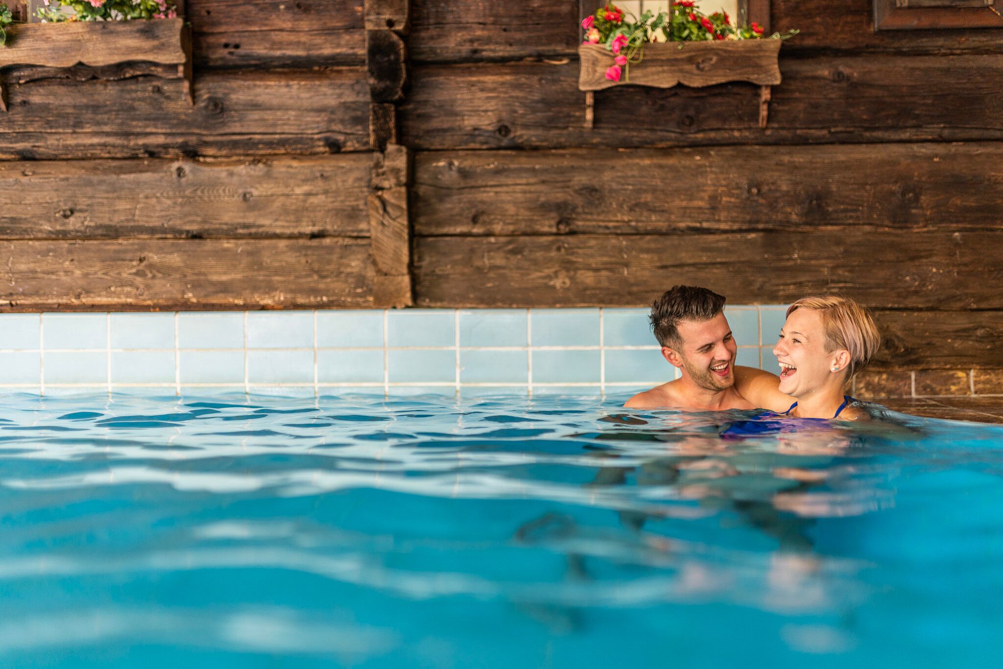 Couple enjoying a relaxing moment in the pool in front of a rustic wooden wall