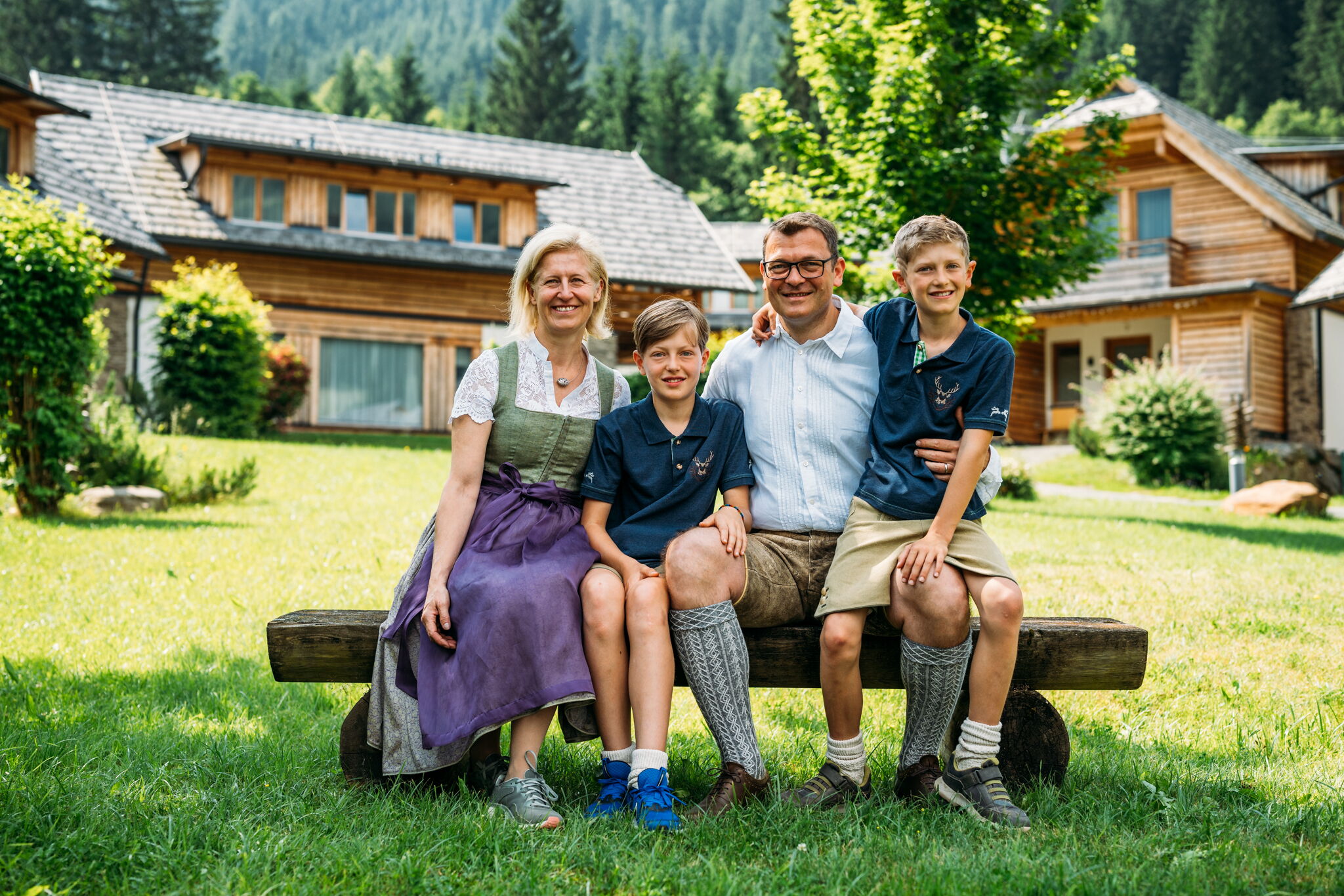 Vierköpfige Familie sitzt fröhlich auf Bank vor malerischen Chalets