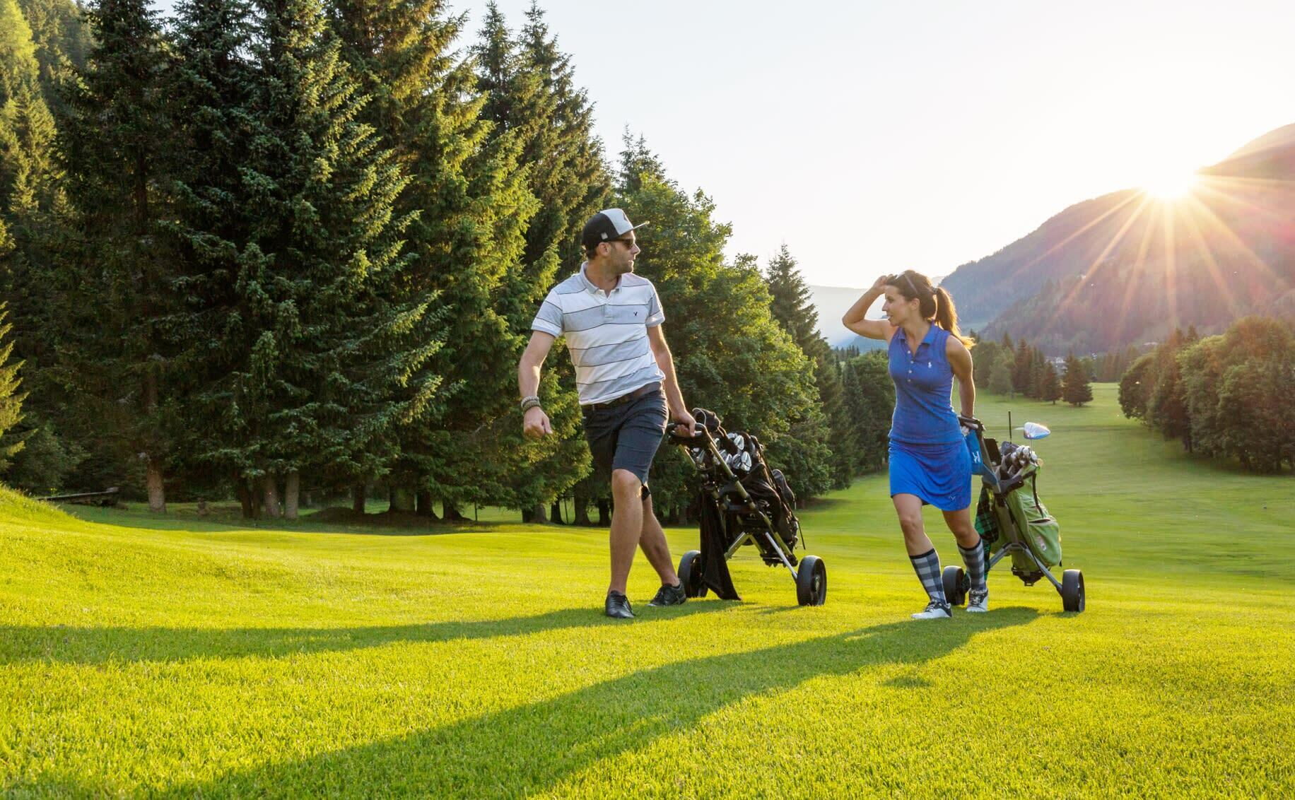 Two people golfing in the sunset against a mountain backdrop.