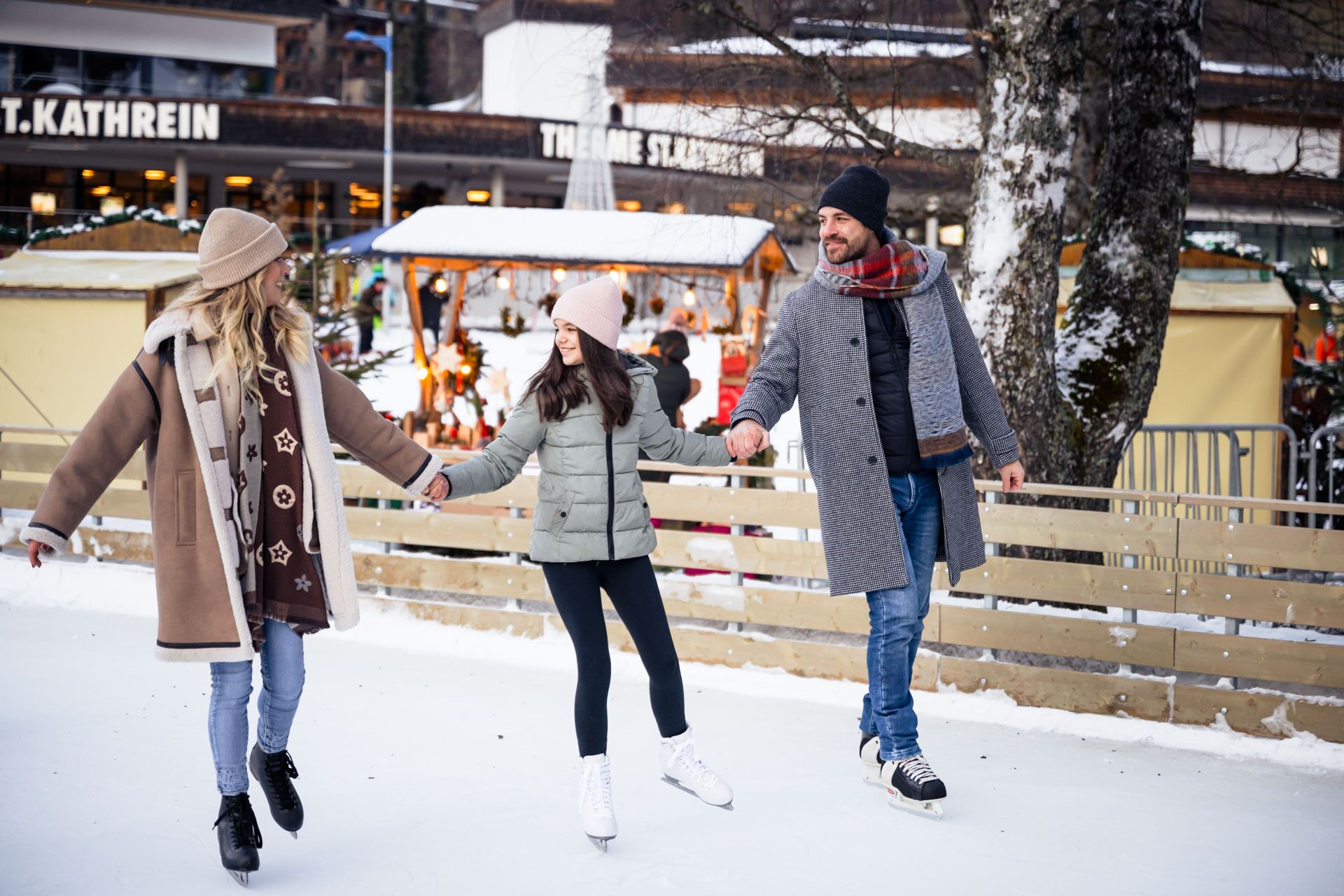 Familie hält Händchen beim Schlittschuhlaufen auf einer winterlichen Eisbahn.