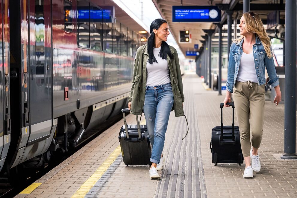 Zwei Reisende ziehen Koffer auf einem Bahnsteig neben einem Zug.