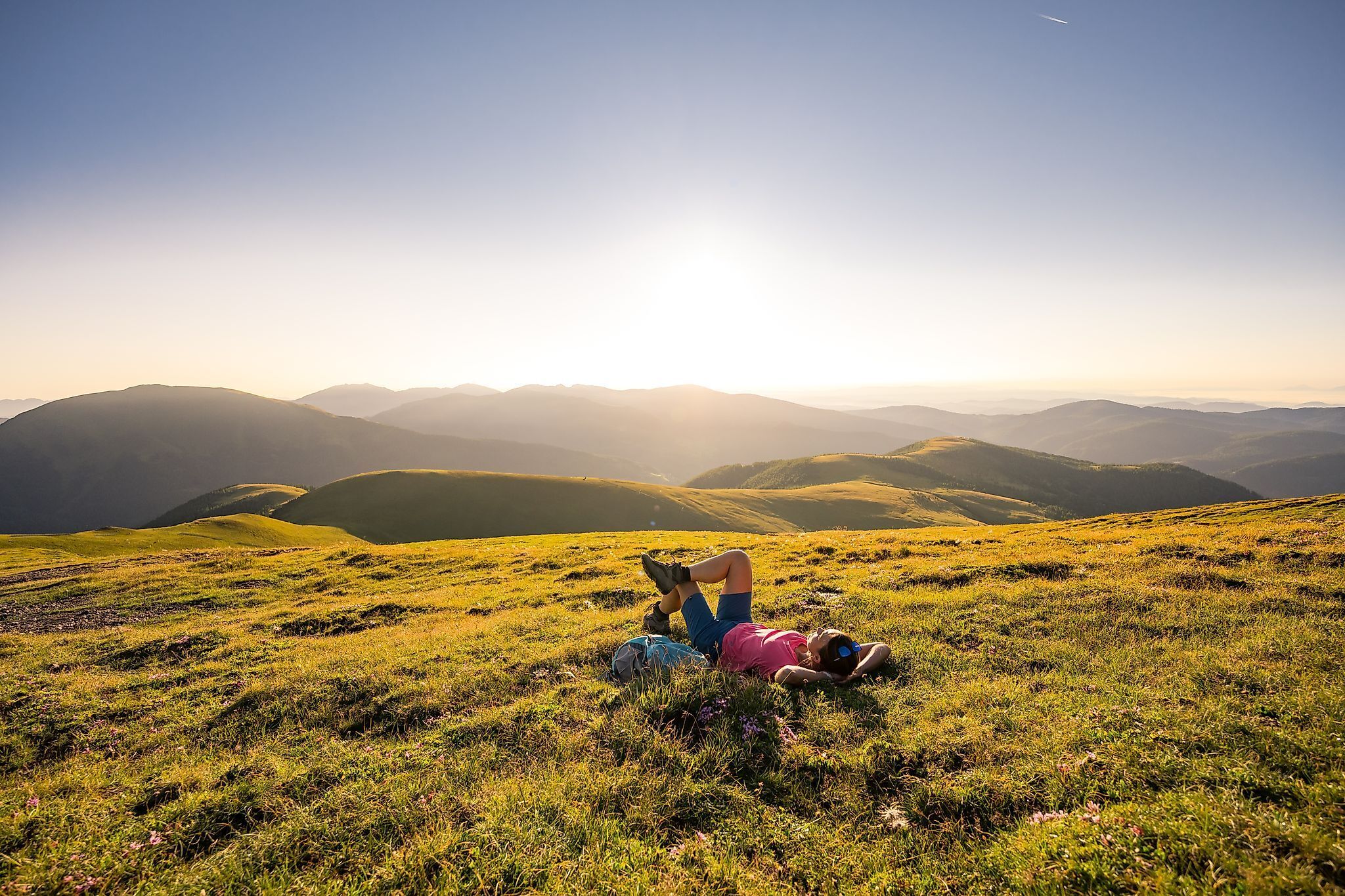 Person relaxing on a meadow in the Nockberge mountains at sunset.