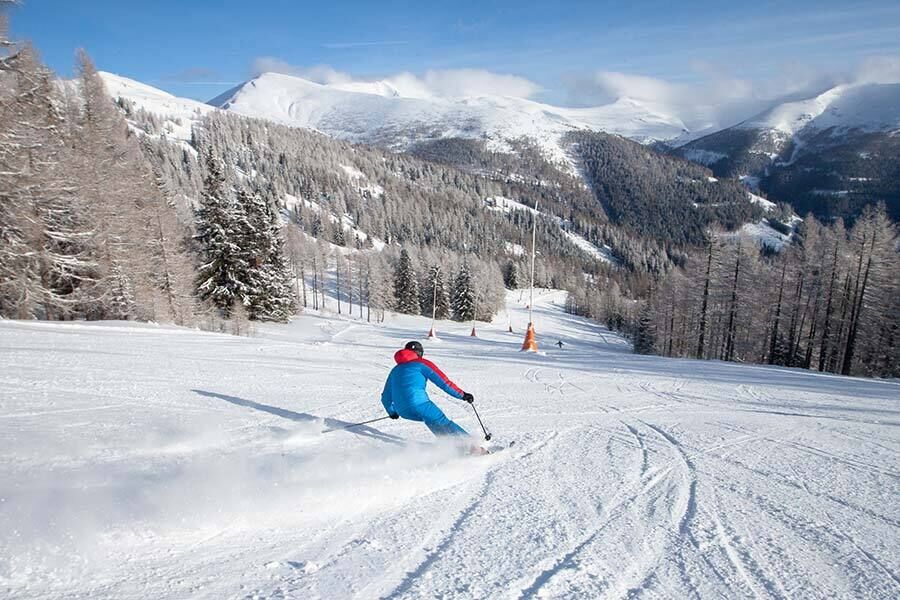 Sciatori su una pista innevata, circondati da montagne e foreste innevate.