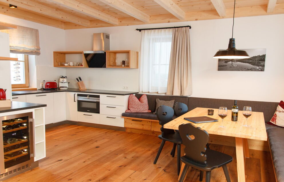 Moderne Holzküche mit Sitzecke, Esstisch, Stühlen und Weingläsern in gemütlichem Chalet.