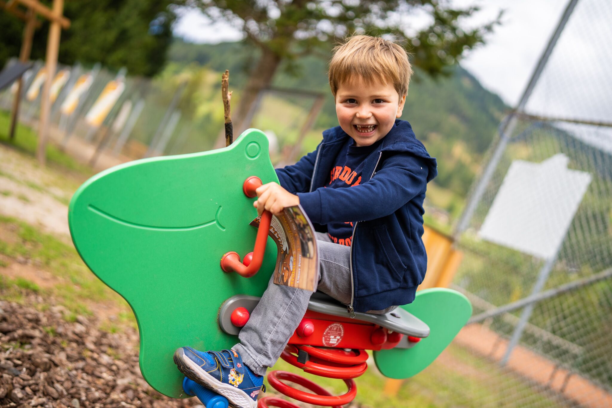 Smiling boy on green outdoor play equipment in sunny weather.