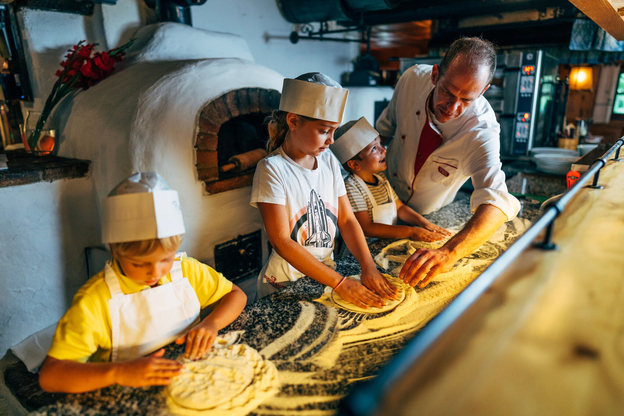I bambini preparano la pizza con un fornaio davanti a un tradizionale forno a legna.