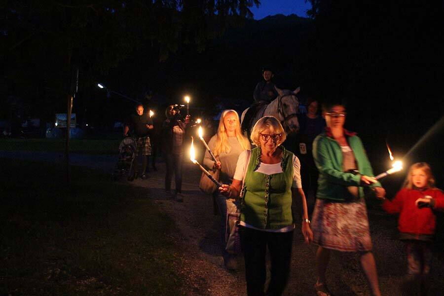 People on a torchlight hike at night with a horse and glowing torches.