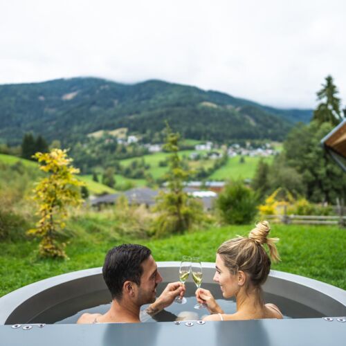 La coppia si gode il relax nella vasca idromassaggio all'aperto con vista sulle montagne Nockberge.